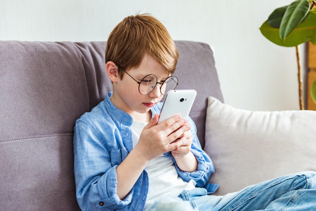 Child boy in glasses plays tablet. Astigmatism, myopia, strabismus, poor vision concept