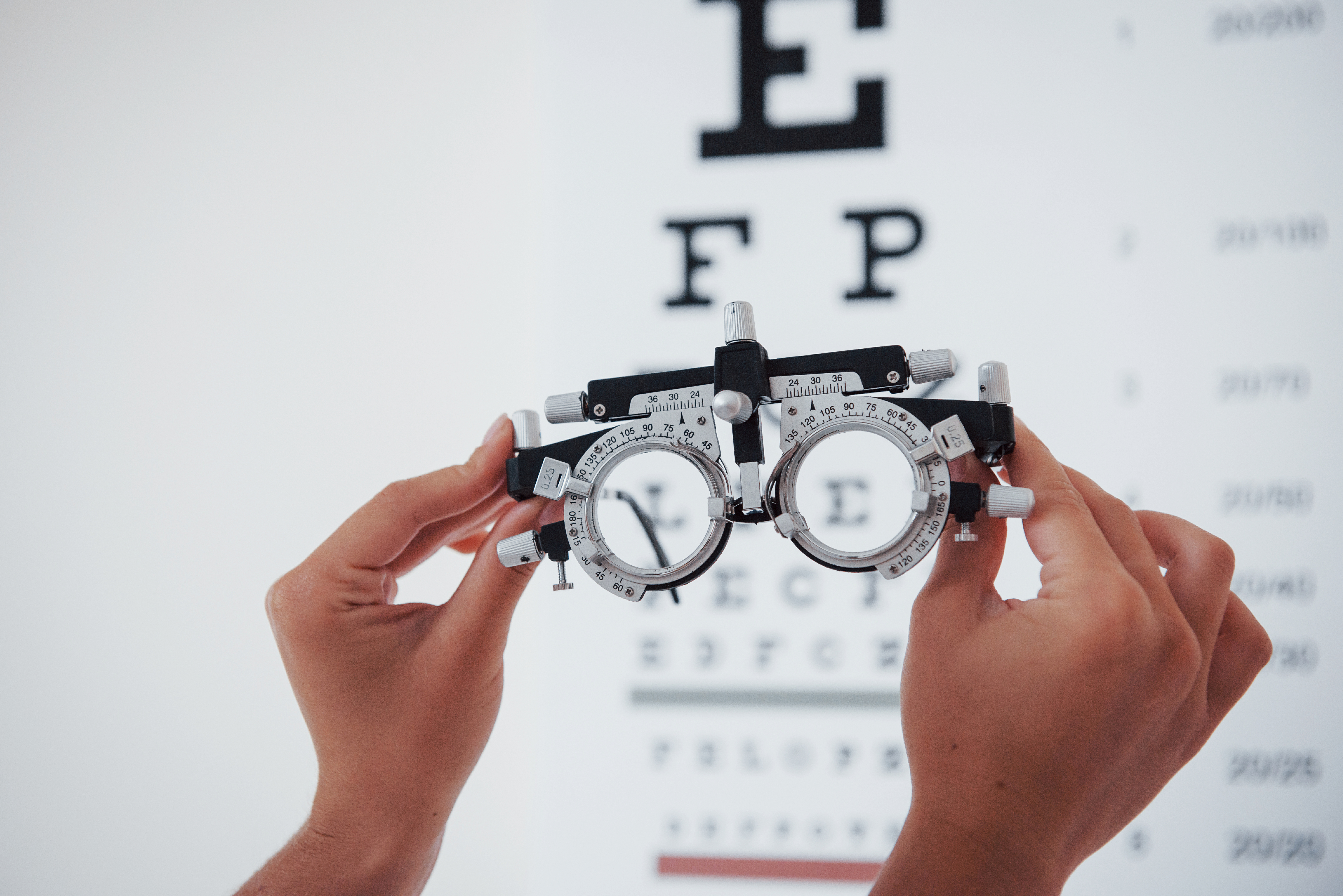Phoropter in the picture. Woman hands holding the glasses on background of the eye chart